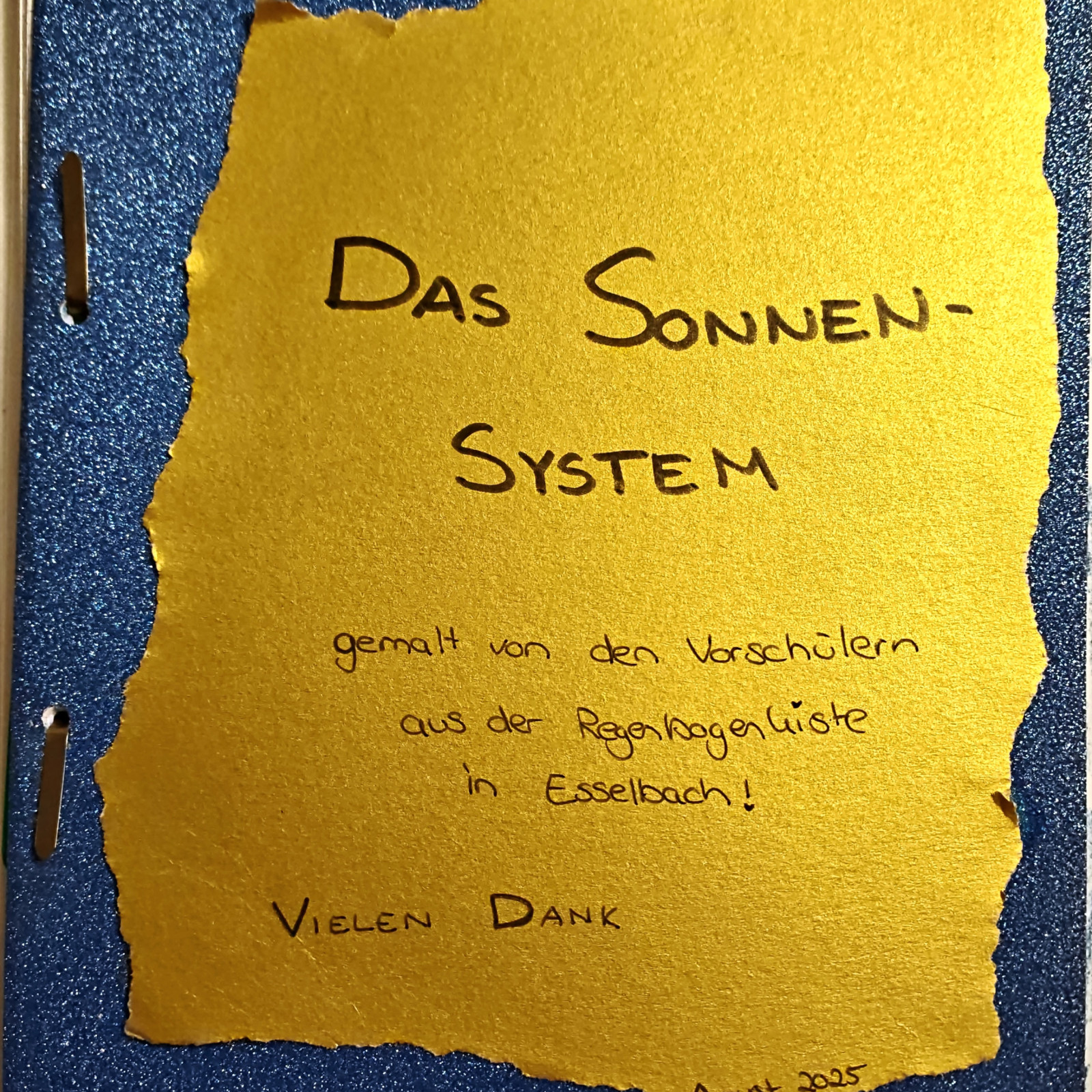 Blauer Ordner mit goldener Papierseite, 'Das Sonnensystem' in handgeschriebener Schrift.