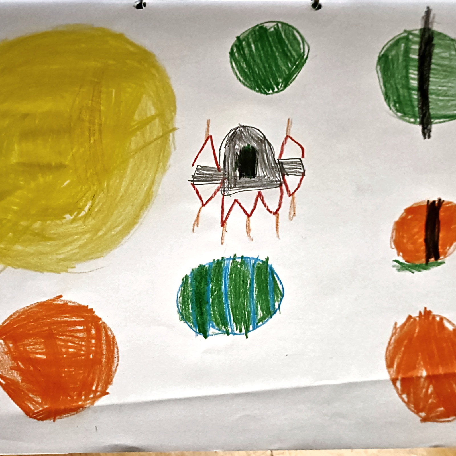 Kinderzeichnung mit mehreren bunten Planeten auf einem weißen Blatt Papier.