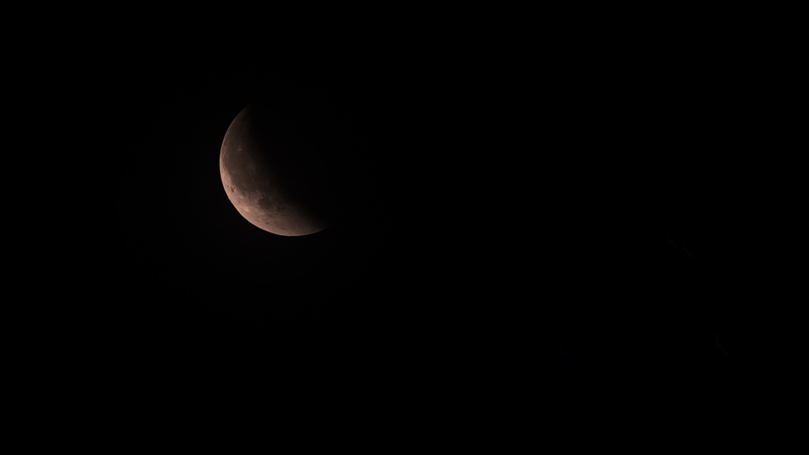 Düstere Mondfinsternis mit einem teilweise beleuchteten Mond vor dunklem Himmel.