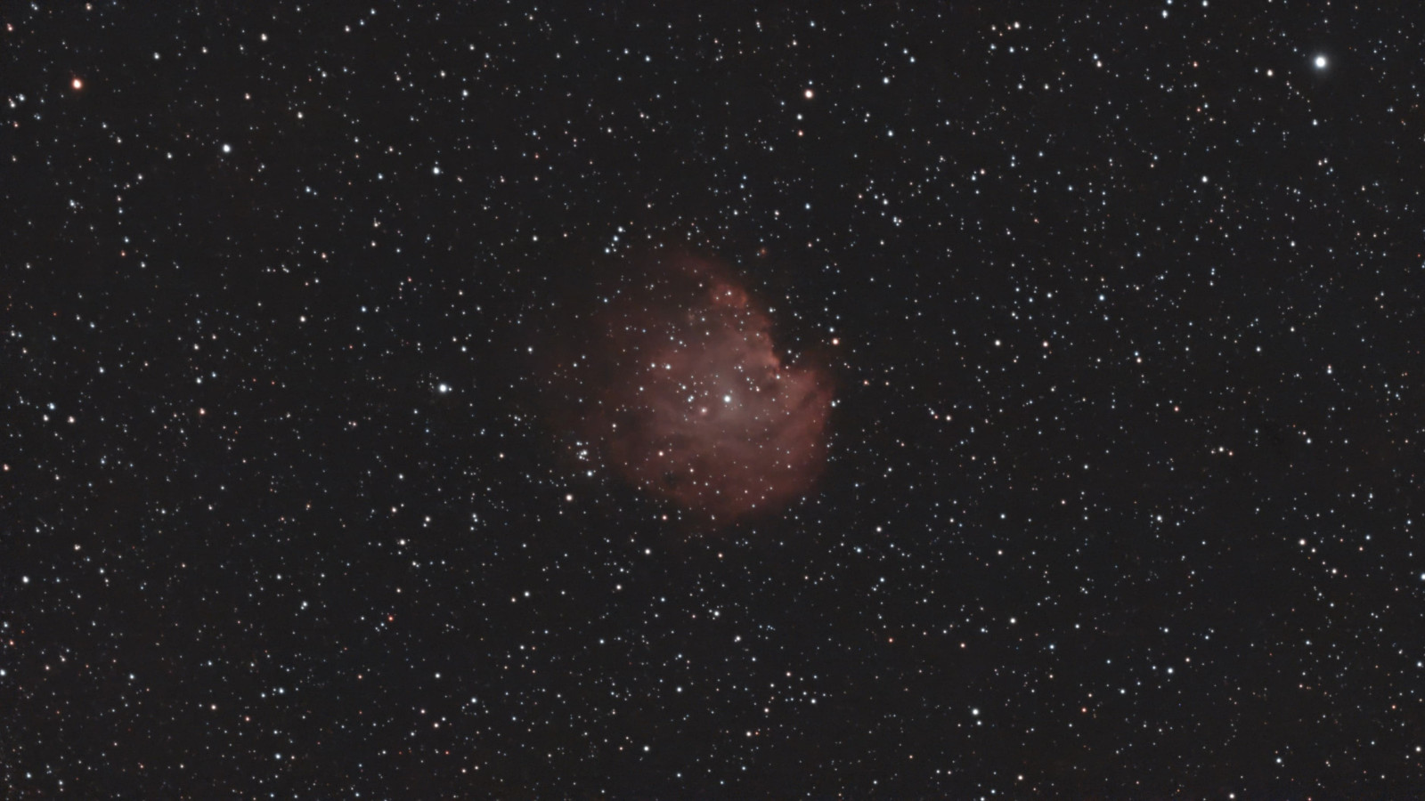 Ein rötlicher Emissionsnebel im Weltraum, umgeben von vielen Sternen.