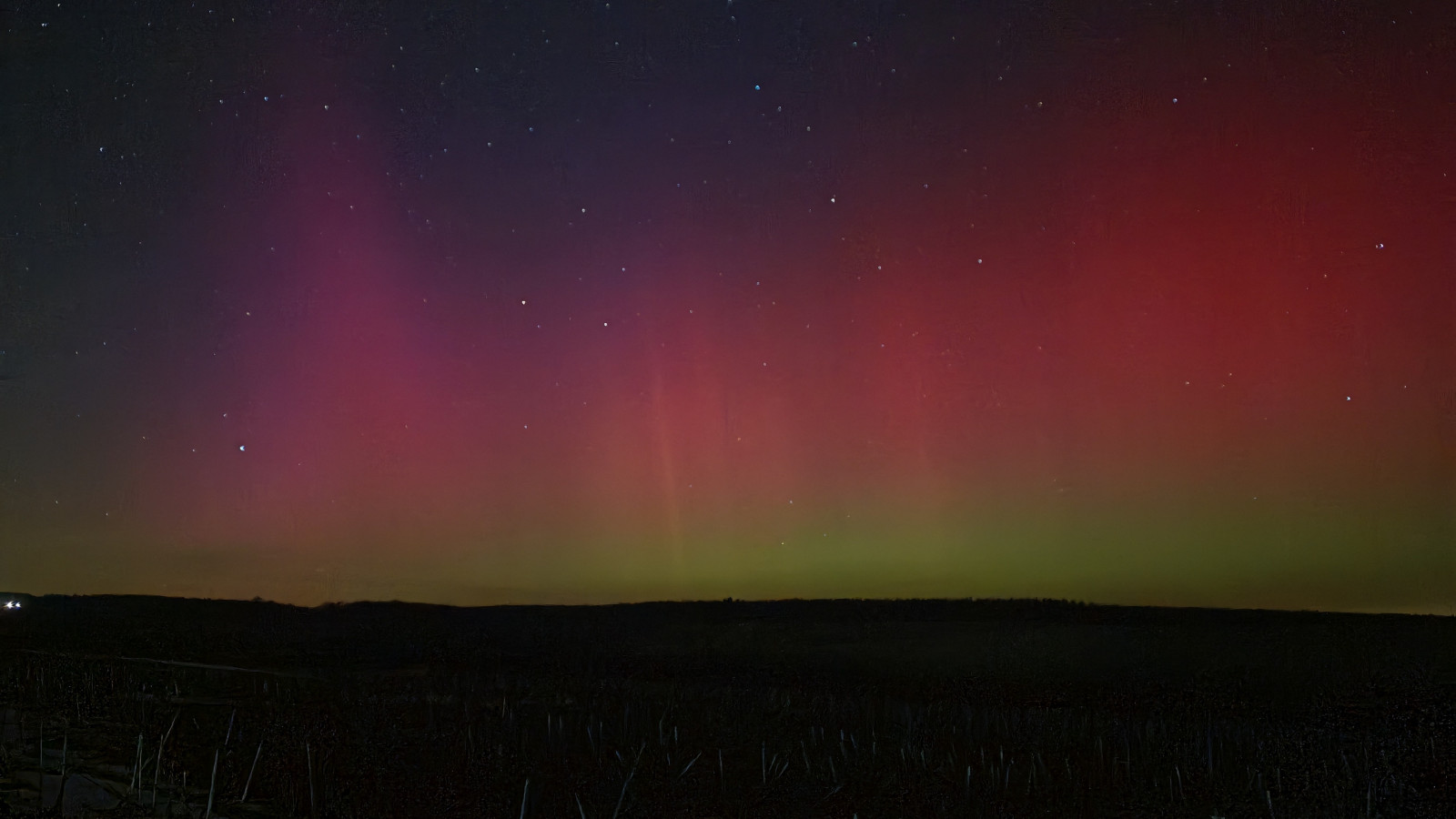 Ein Nordlicht in Violett und Rot leuchtet am Himmel über einer dunklen Landschaft, umgeben von Sternen.