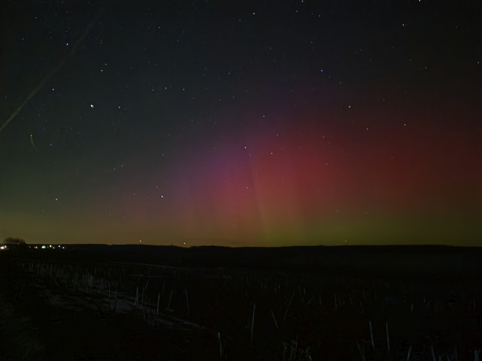 Polarlichter in Rottönen, die nachts den Himmel über einer Landschaft erleuchten.