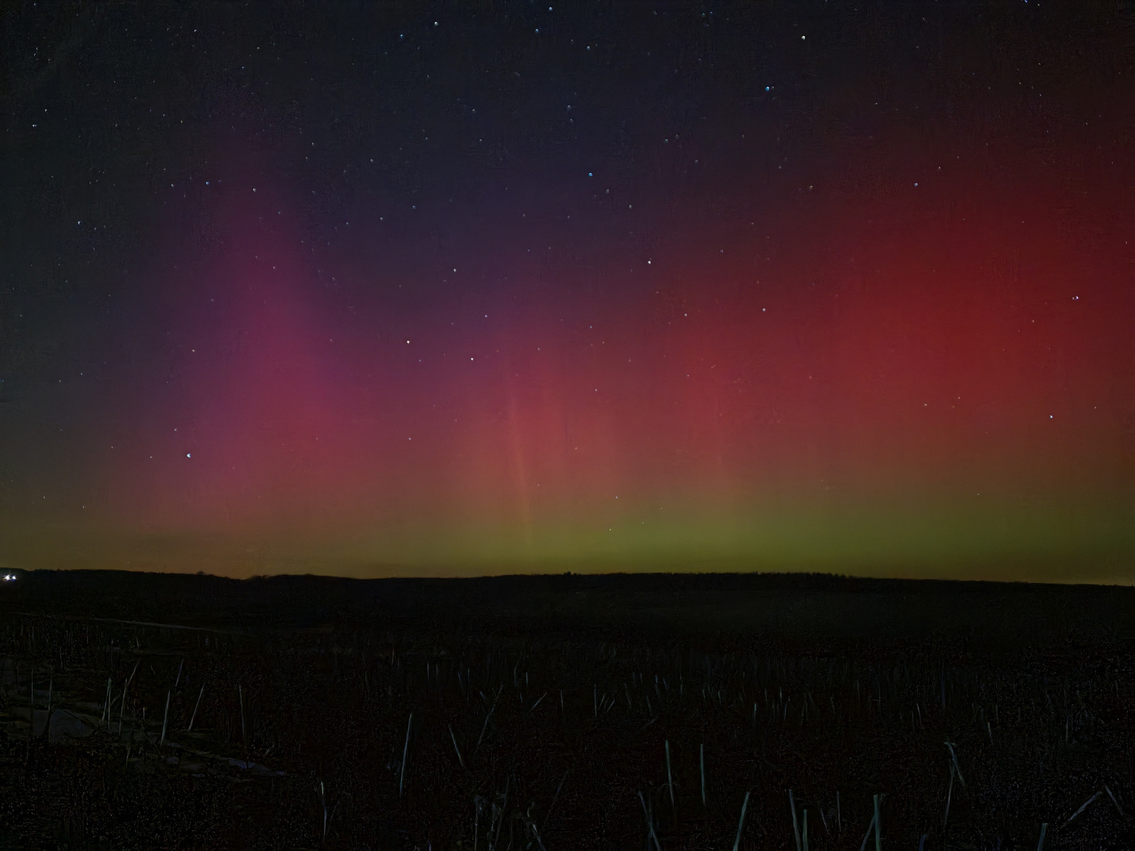 Rote und grüne Nordlichter am Nachthimmel über einer dunklen Landschaft.