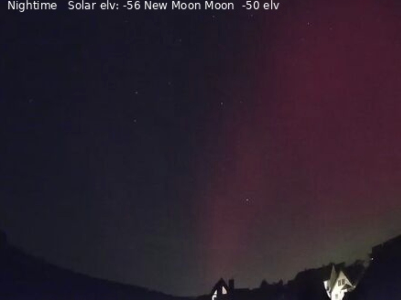Nachthimmel mit rosa Aurora über einer Landschaft mit Gebäuden.