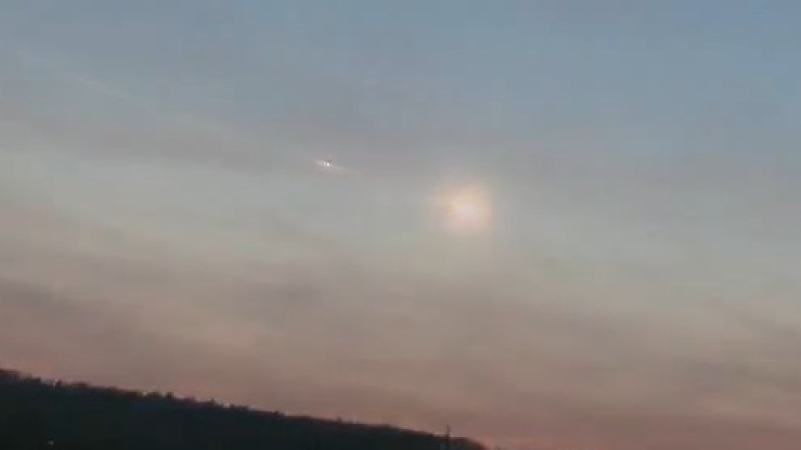 Ein Abendhimmel mit einem leuchtenden Phänomen über einer dunklen Hügelkette am Horizont.